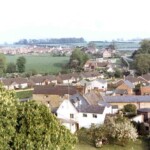 View of School Lane from the Church Tower, c1970s. Perry Lane is situated beyond the field in the middle distance. The current school is behind the Old School House to the right of the field. The white building in the foreground is Calgary House in Church End. View of School Lane from the Church Tower, c1970s